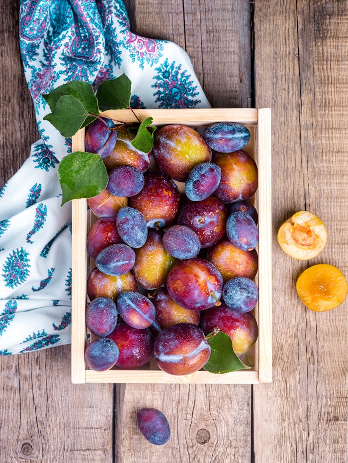Vibrant fresh plums in a wooden crate on rustic table, perfect for healthy eating themes.